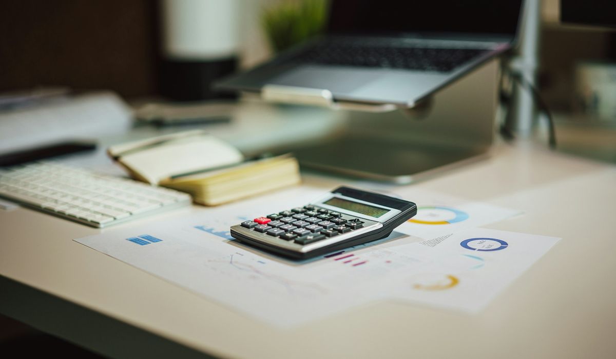 Calculadora sobre relatórios financeiros em uma mesa de escritório, com teclado e notebook ao fundo