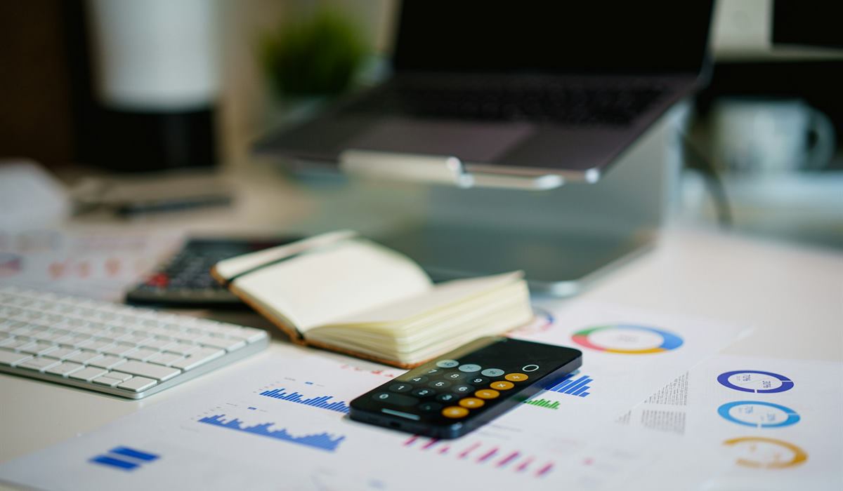 Mesa de escritório com calculadora, caderno e relatórios financeiros impressos